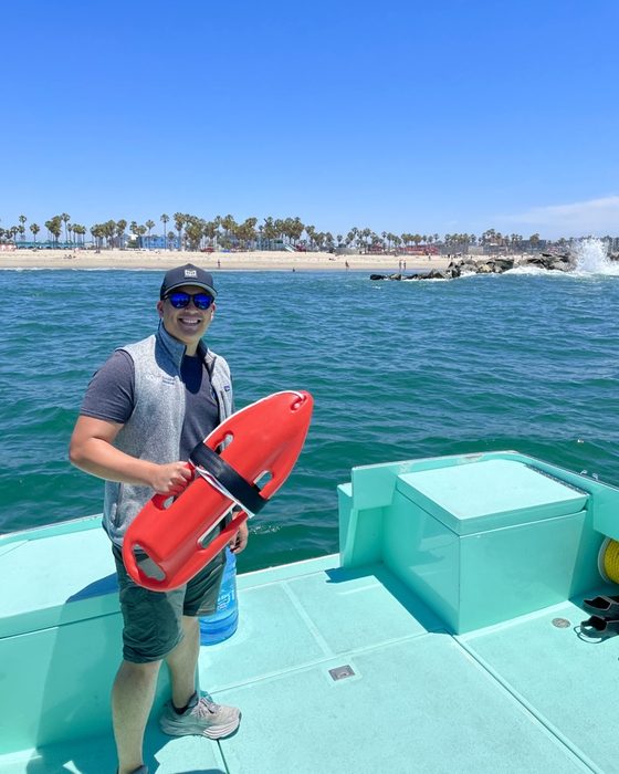 Matt on the deck of a boat off the beach, holding a red rescue buoy