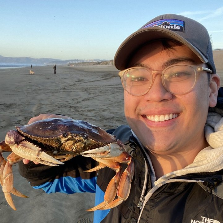 Matt smiling on a beach, holding up a large crab