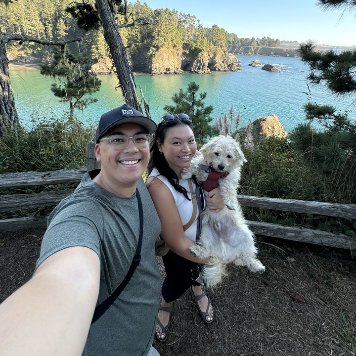 Matt, his partner, and their dog above a turquoise cove