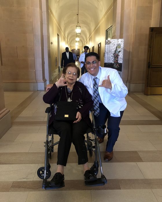 Matt in his white coat crouching beside his grandmother, both making a shaka sign